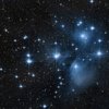 The Pleiades star cluster, also known as the Seven Sisters, showing bright blue stars surrounded by nebulous gas and dust.