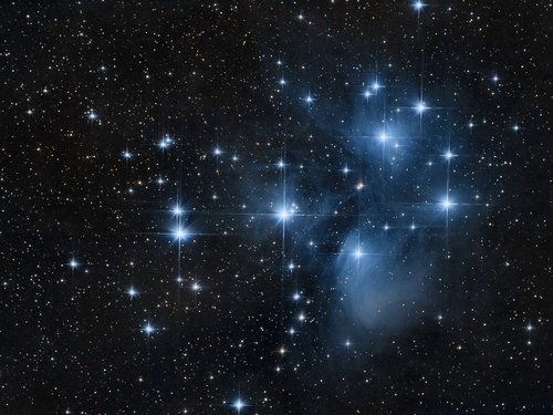 The Pleiades star cluster, also known as the Seven Sisters, showing bright blue stars surrounded by nebulous gas and dust.
